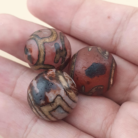 Three round, polished beads with natural stone patterns in reddish-brown, beige, and black, resting on an open hand.