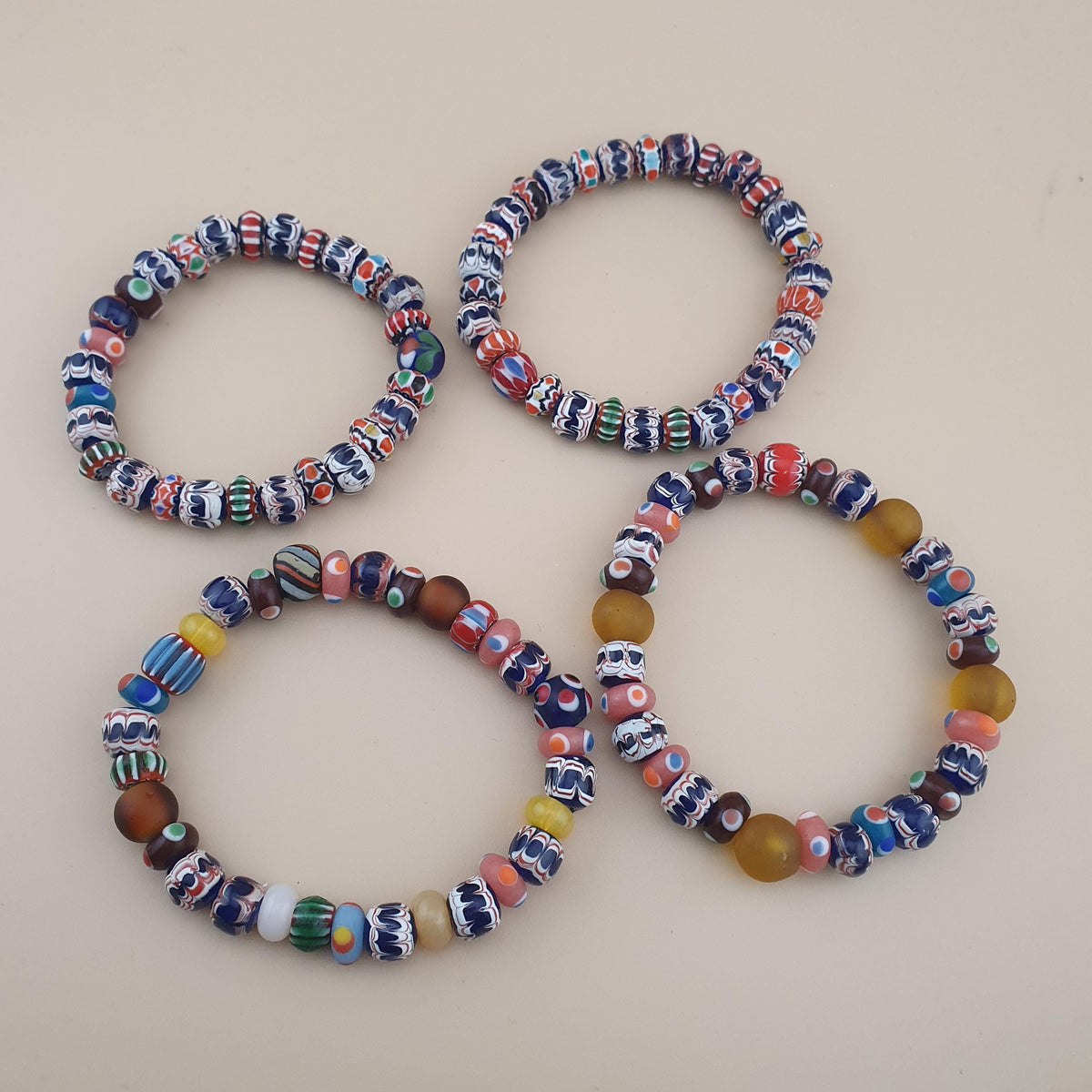 Four beaded stretch bracelets with colorful glass beads, arranged on a light beige background.