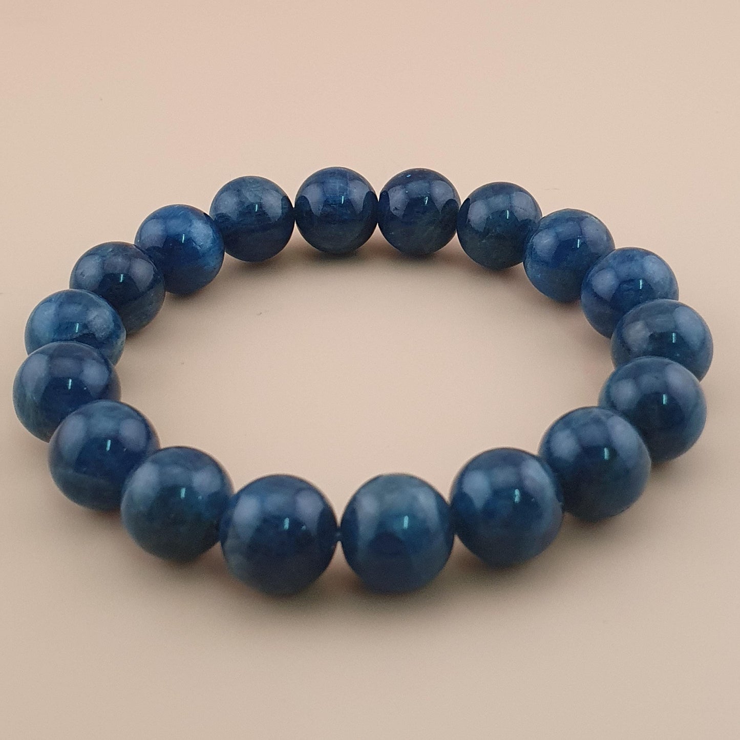 A beaded stretch bracelet made of polished dark blue round beads, displayed on a solid light beige background.