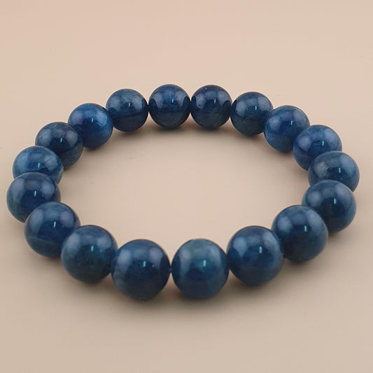 A beaded stretch bracelet made of polished dark blue round beads, displayed on a solid light beige background.